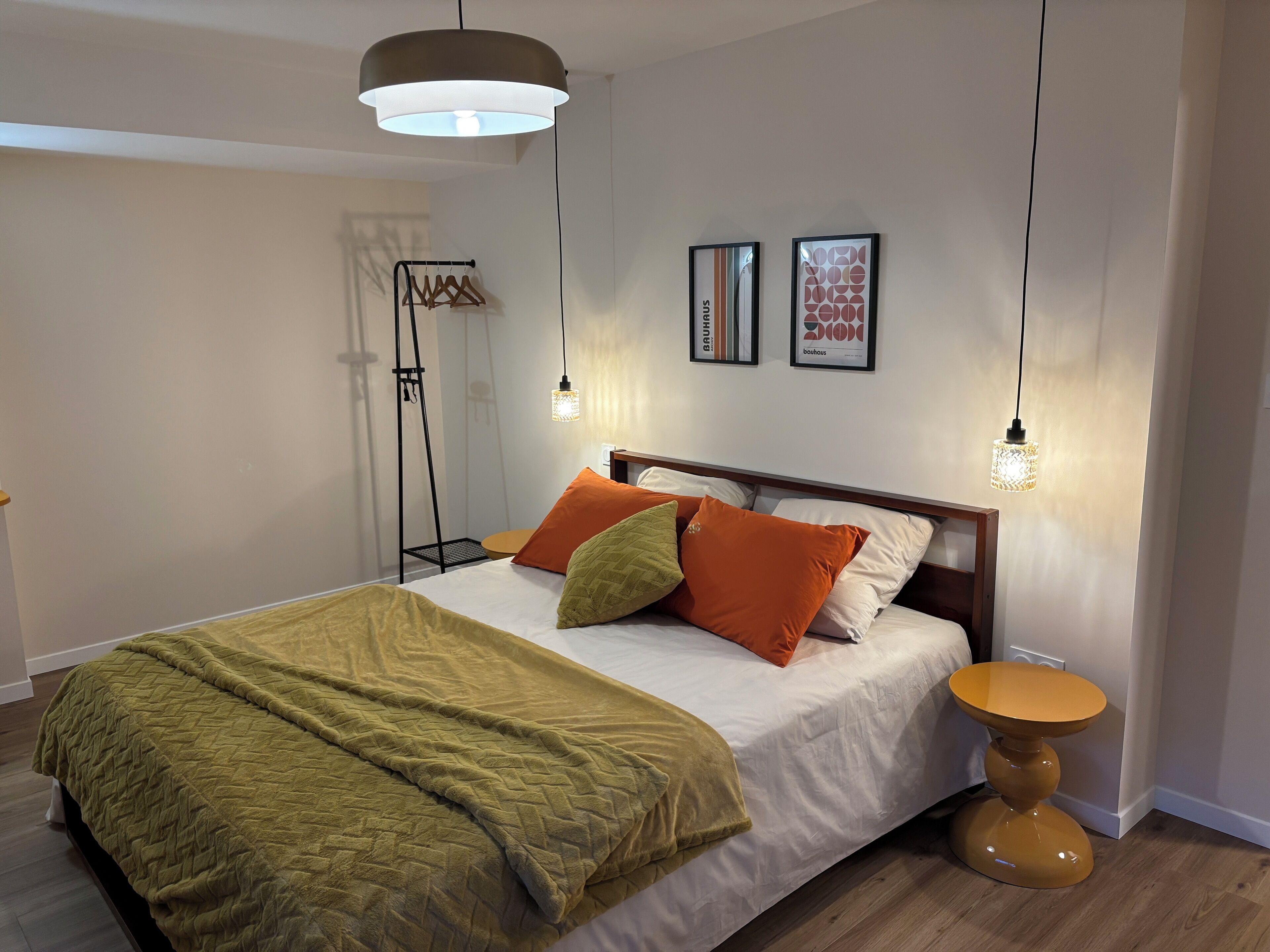 A neatly made bed with a green blanket, a wooden bedside table, and two wall-mounted lights.