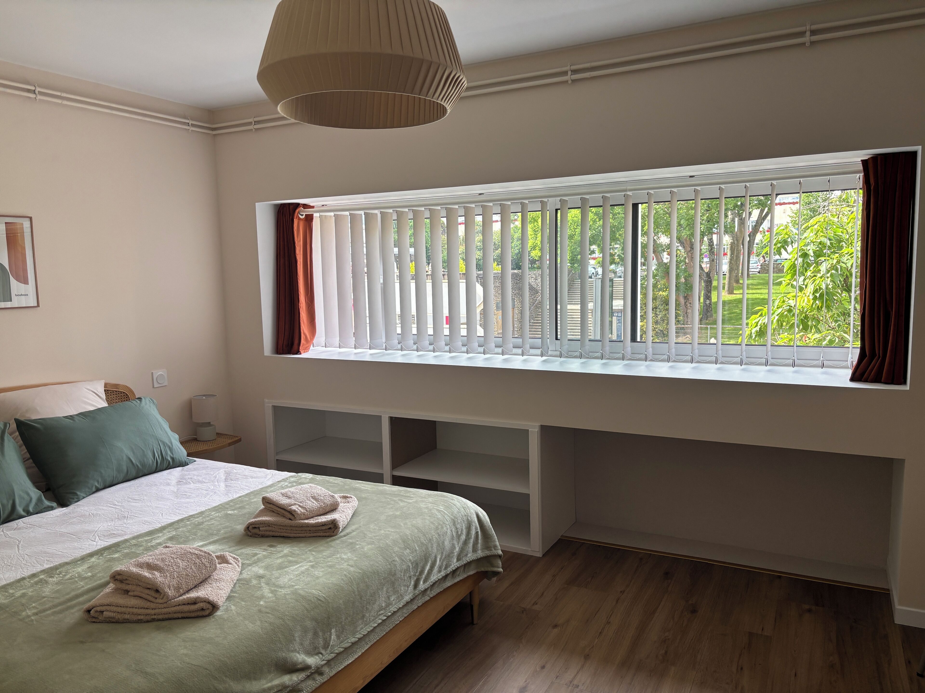 A bedroom with a bed, a window with blinds, a bedside table, and a lamp.