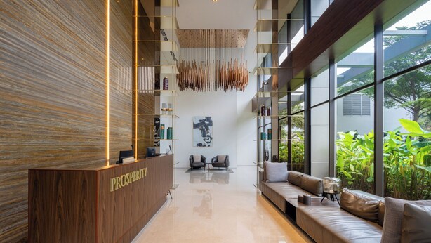 A reception area with a wooden reception desk, seating area, and large windows offering a view of greenery. - Morich Suites Penthouse (Jakarta)