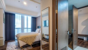 A modern hotel room with a large bed, a walk-in closet, and a large window with curtains. - Morich Suites Penthouse (Jakarta)