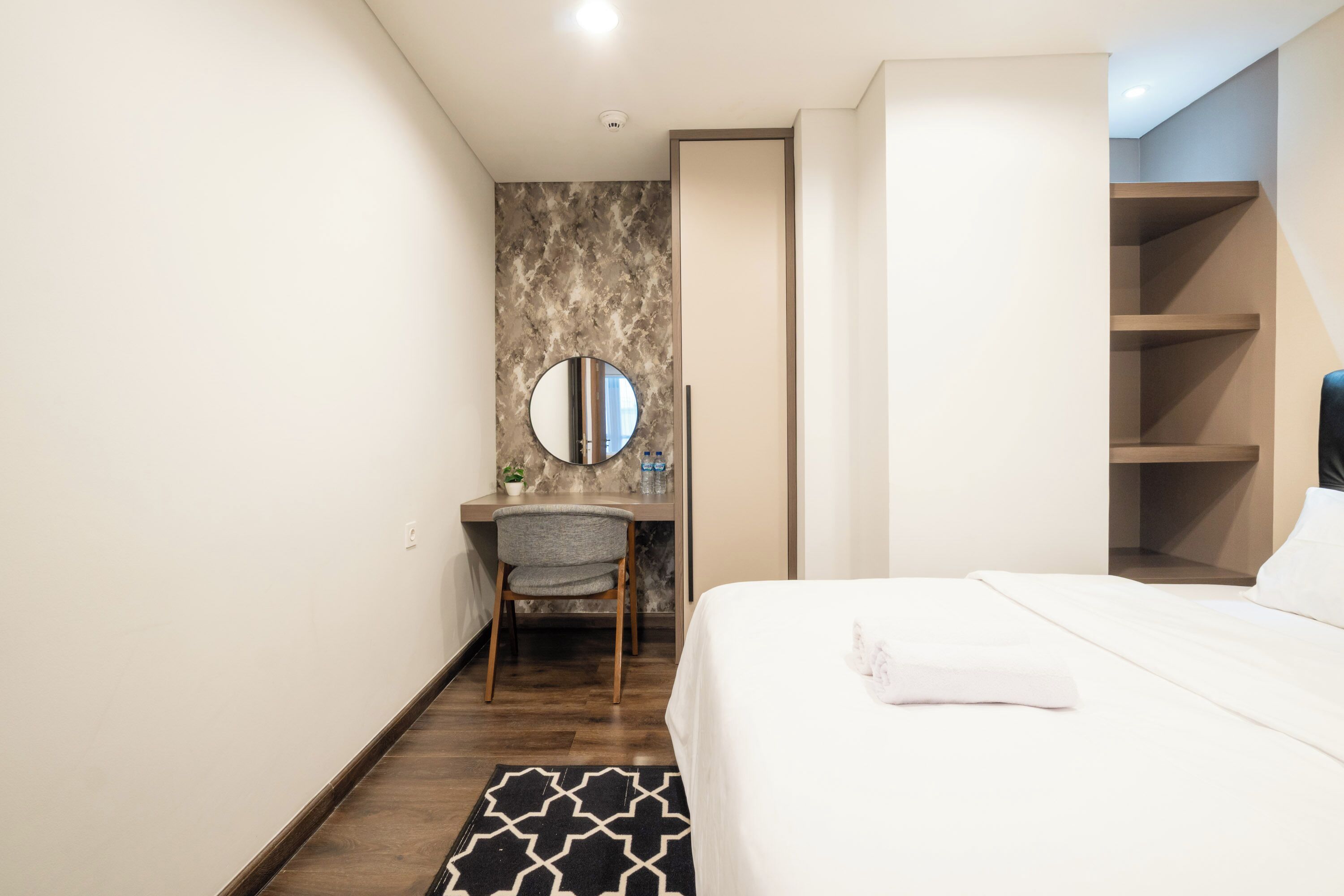 Een hotelkamer met een bed, een bureau met stoel, een ronde spiegel en een kledingkast.