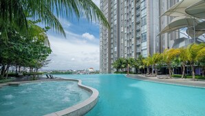 A swimming pool with a curved edge, surrounded by palm trees and lounge chairs. - Morich Suites Penthouse (Jakarta)