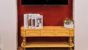 Ein Fernseher an einer roten Wand, darunter eine Holzkonsole.