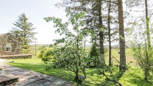 En bygning i sten med en stenkø ved et græsareal med træer og udsigt over landskabet.
