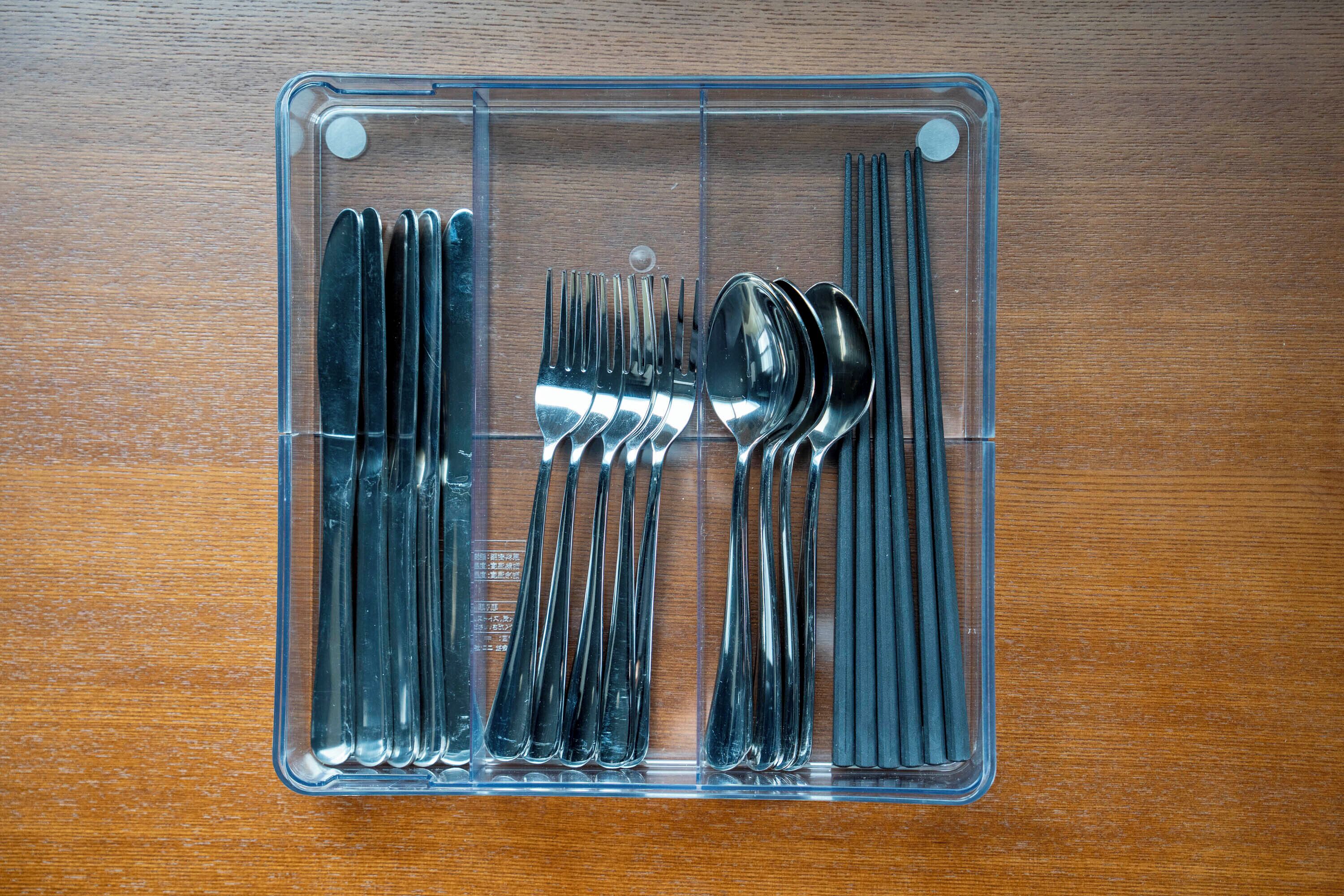 A clear plastic storage organizer with utensils neatly arranged inside.