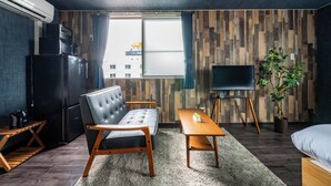 Habitación de hotel moderna con sofá, una mesita, televisor, planta y vista a la ciudad por la ventana.