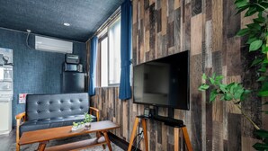 Una sala de estar moderna con un sofá negro, una mesa de centro de madera y un televisor sobre un mueble.