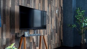 Un televisor sobre un mueble de madera en una habitación con pared de madera y una planta en maceta.