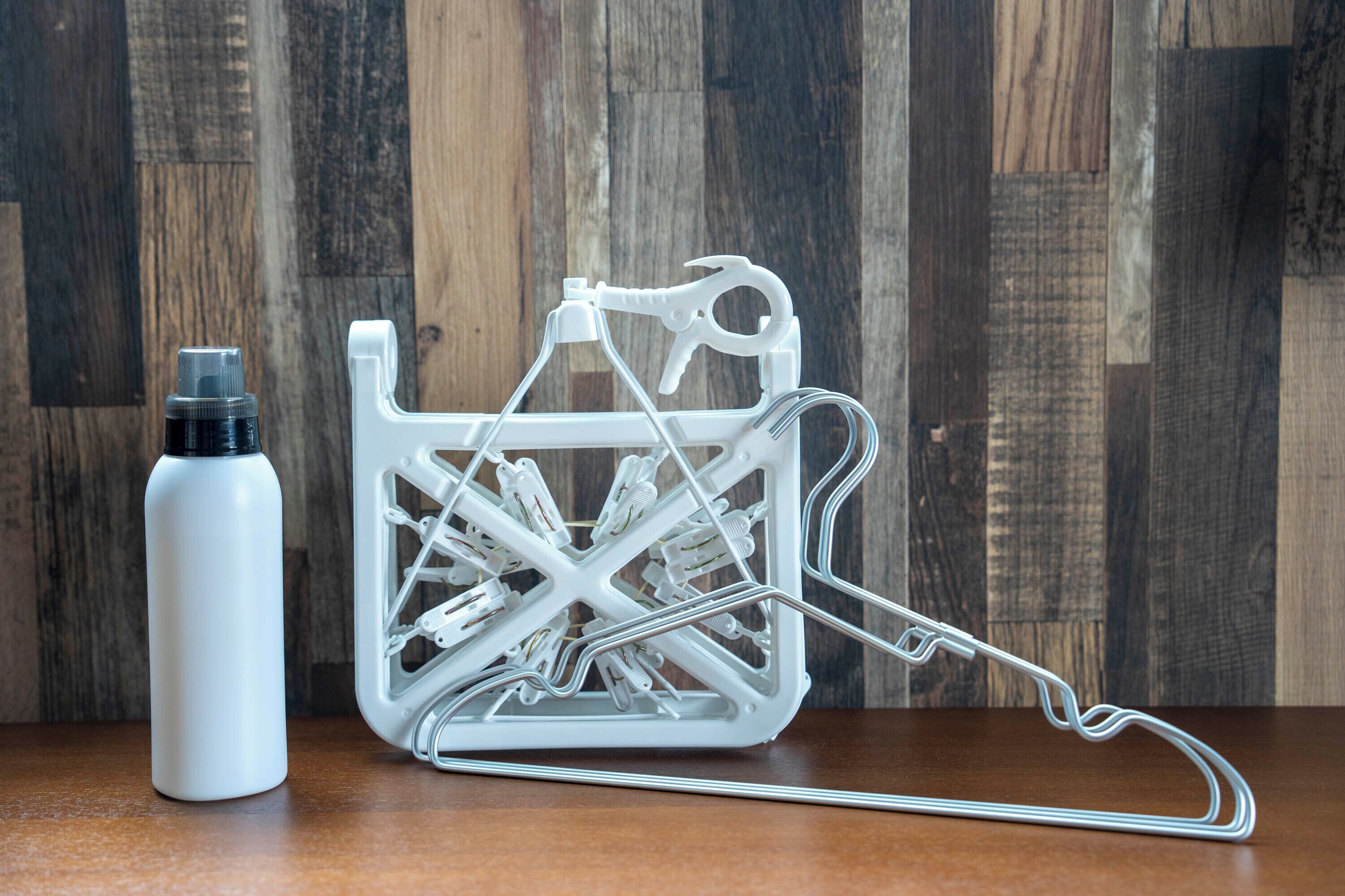 A white plastic laundry basket with metal hangers and a white bottle on a wooden surface.