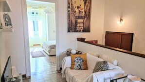 A well-lit room with a bed, a sofa with patterned cushions, a painting of a street scene, and a wooden cabinet. - Relax in this quiet space just a stone's throw from Tesoriera Park. (Torino)