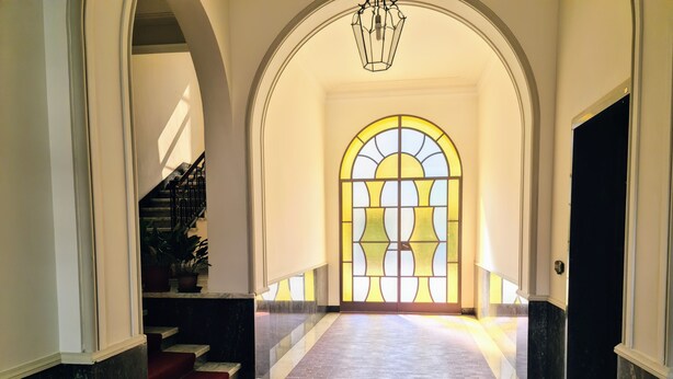 A grand hallway with a marble floor, a staircase with red carpet, and a large arched window with stained glass. - Relax in this quiet space just a stone's throw from Tesoriera Park. (Torino)