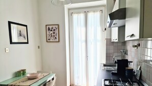 A kitchen with a gas stove, a dining table with chairs, a window with curtains, and framed artwork on the wall. - Relax in this quiet space just a stone's throw from Tesoriera Park. (Torino)