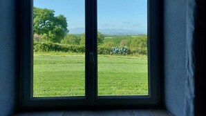 Ein Zimmer mit großem Fenster und Blick auf ein grünes Feld und ferne Hügel.