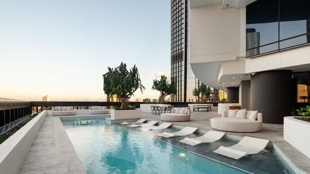 A rooftop pool area with lounge seating and a view of the city skyline.