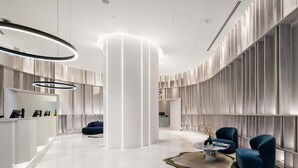 A modern lobby with a central white pillar, seating area with blue chairs, and a reception desk.