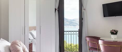 Un dormitorio con cama, escritorio, silla, televisor y balcón con vistas a las montañas.
