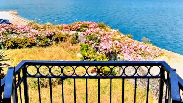 A coastal view with mountains in the background, a balcony with a railing, and a flower bed with pink flowers. - Domus Vittorio double room with balcony and sea view  (Gaeta)