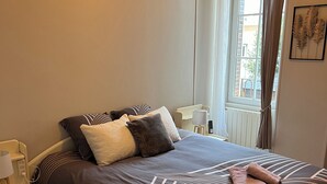 Una cama bien hecha con ropa de cama a rayas, una mesita de noche con lámpara y una ventana con cortinas.