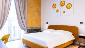 A hotel room with a large bed, a yellow chair, a desk, and a view of the outside through a window with curtains. - Guest House Le Sei Porte   Porta Elina (Salerno)