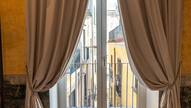 A room with a view through a glass door, curtains tied at the bottom, and a balcony with railings. - Guest House Le Sei Porte   Porta Elina (Salerno)