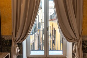 Une pièce avec une vue dégagée sur l’extérieur, accessible par une porte vitrée, des rideaux attachés en bas et un balcon doté de balustrades.