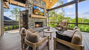A stone fireplace with a TV above it, outdoor seating, and a view of the landscape. - Lost Bark Lodge at Eagles Nest Great Camp, hot tub, pool table, fenced yard (Banner Elk)
