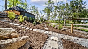 A rustic cabin with a wooden exterior and a sloped roof, surrounded by a well-maintained garden with stone pathways and a wooden fence. - Lost Bark Lodge at Eagles Nest Great Camp, hot tub, pool table, fenced yard (Banner Elk)