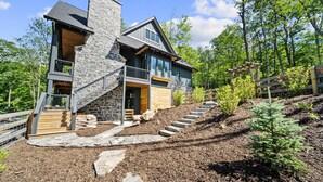 A modern two-story house with a stone facade, wooden deck, and a stone staircase leading to the entrance. - Lost Bark Lodge at Eagles Nest Great Camp, hot tub, pool table, fenced yard (Banner Elk)