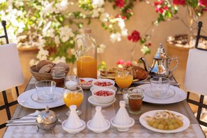 A breakfast table set with various dishes, including bread, fruit, and beverages, in a sunny outdoor setting. - Riad Noasid  (Marrakech)