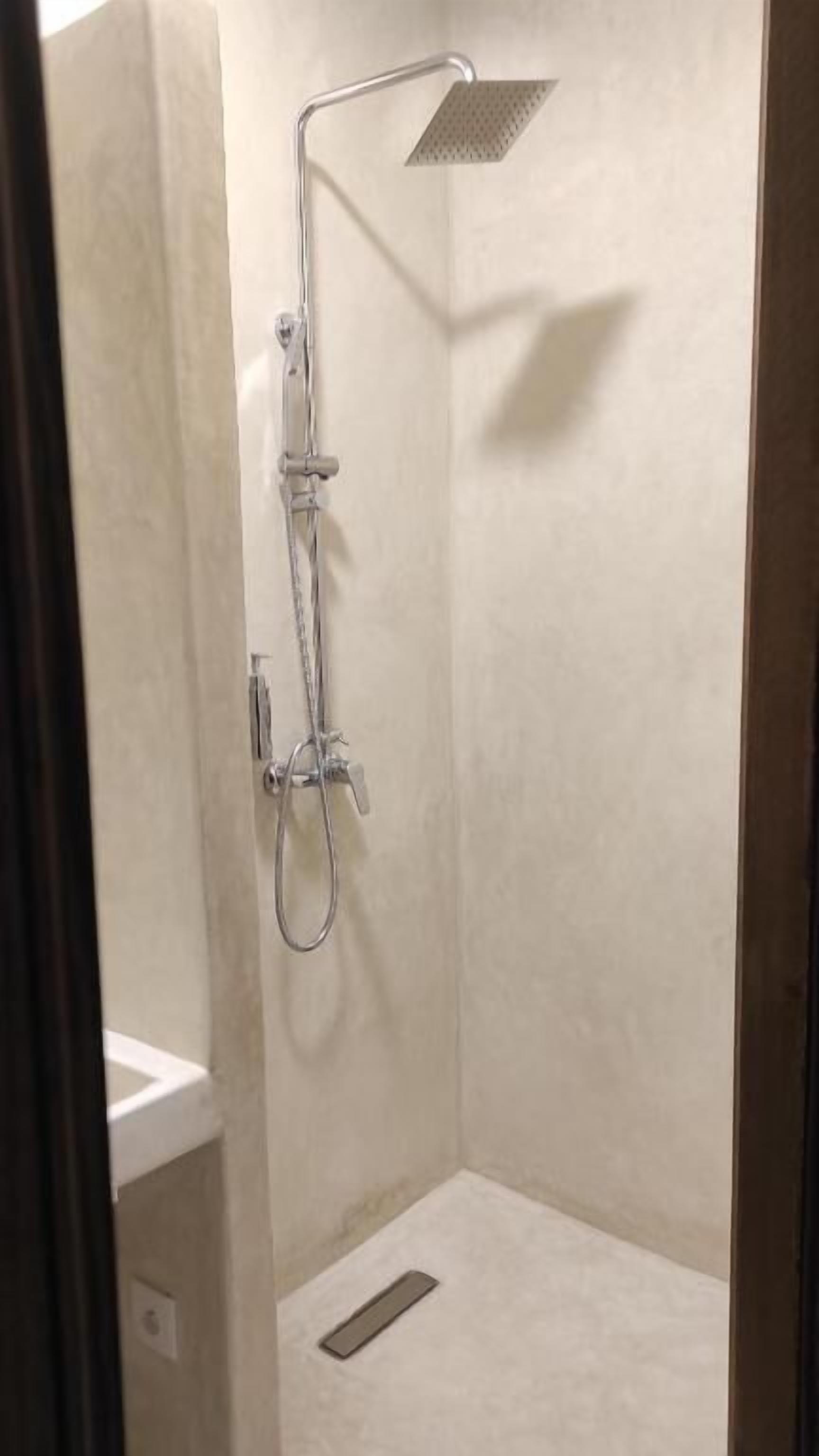 A small, enclosed shower area with a handheld showerhead and a fixed showerhead.