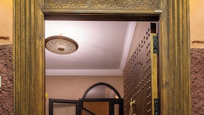 Un couloir avec un tapis à motifs, une porte en bois ornée de clous en laiton et un luminaire suspendu.