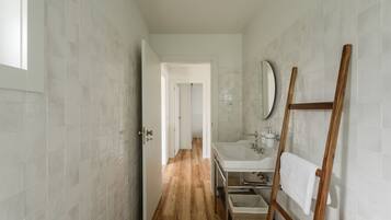 A narrow hallway with a wooden floor leading to a bathroom with a sink and mirror.