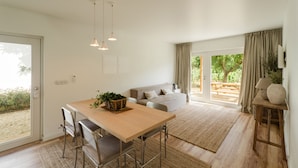 Una cocina moderna con una mesa de madera, taburetes de bar, luces colgantes y vista al jardín a través de un gran ventanal corredera.