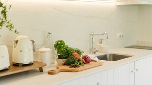 A kitchen with a marble countertop, a wooden cutting board with vegetables, a white kettle, and a potted plant. - Imago Houses 3 - by MET (Lamego)
