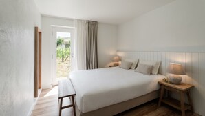 A bedroom with a large bed, bedside lamps, a wooden bench, and a view of greenery through a door. - Imago Houses 3 - by MET (Lamego)