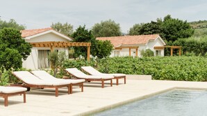 Zona de piscina con sillones de descanso y un edificio con tejado de azulejos.