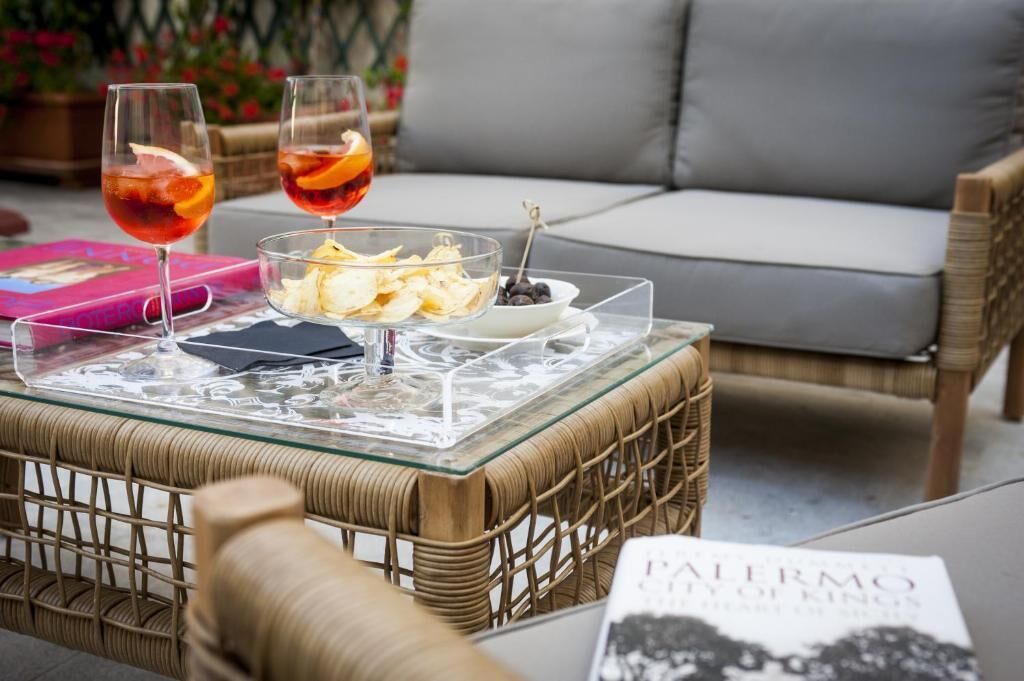 A glass table with two drinks, a bowl of snacks, and a book titled "Palermo City of Kings".
