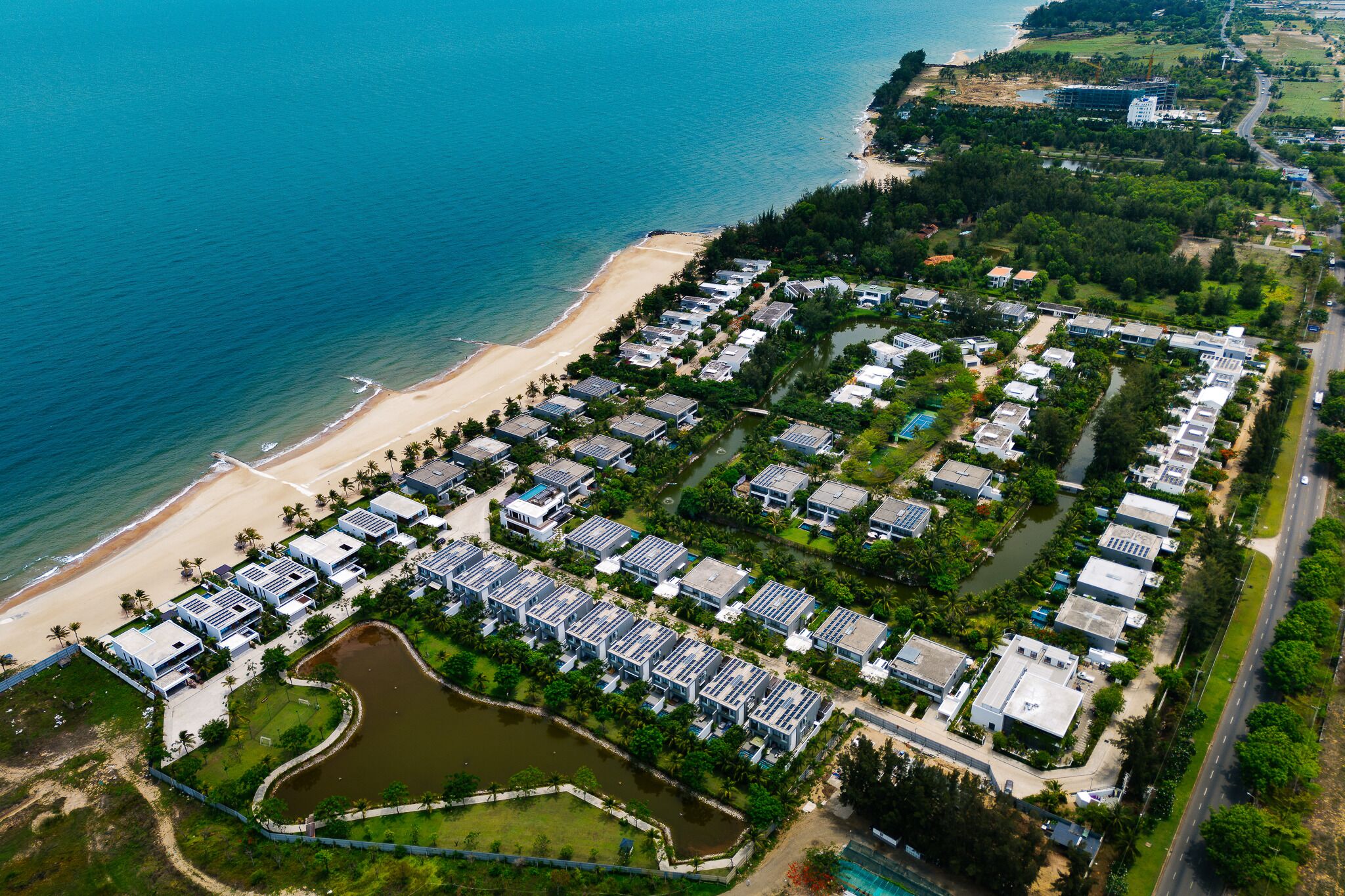 Vista aérea de um resort costeiro com vários edifícios, uma praia e um rio.