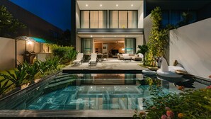 Una casa moderna con piscina, mobiliario exterior y una terraza bien iluminada.