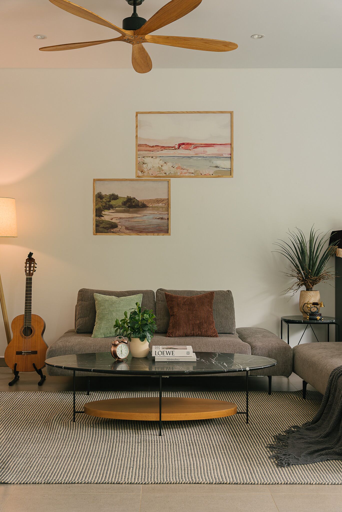 En stue med sofa, sofabord og en guitar. To malerier hænger på væggen, og der er en plante på et sidebord.