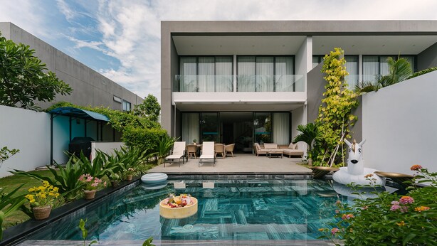 Una casa moderna con piscina, mobiliario exterior y abundante vegetación.