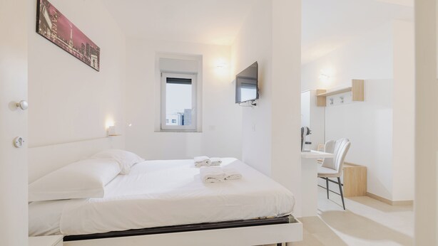 A modern hotel room with a neatly made bed, a flat-screen TV mounted on the wall, and a small desk with a chair. - Double bed and sofa bed with private bathroom 3-4 people - 20 minutes from Milan (Trezzano sul Naviglio)