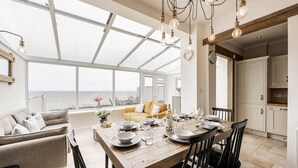 Un comedor con una mesa de madera dispuesta para cuatro personas, un sofá y vista al mar a través de amplios ventanales.