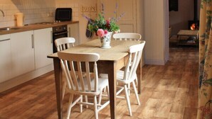 A cozy kitchen with wooden flooring, a dining table with chairs, a hanging pendant light, and a visible fireplace in the background. - Set in the stunning grounds of Bayfield Hall (Bayfield)
