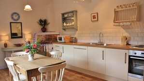 A kitchen with white cabinets, a wooden countertop, a microwave, a sink, and a stove. There is a dining table with chairs and a vase of flowers. - Set in the stunning grounds of Bayfield Hall (Bayfield)