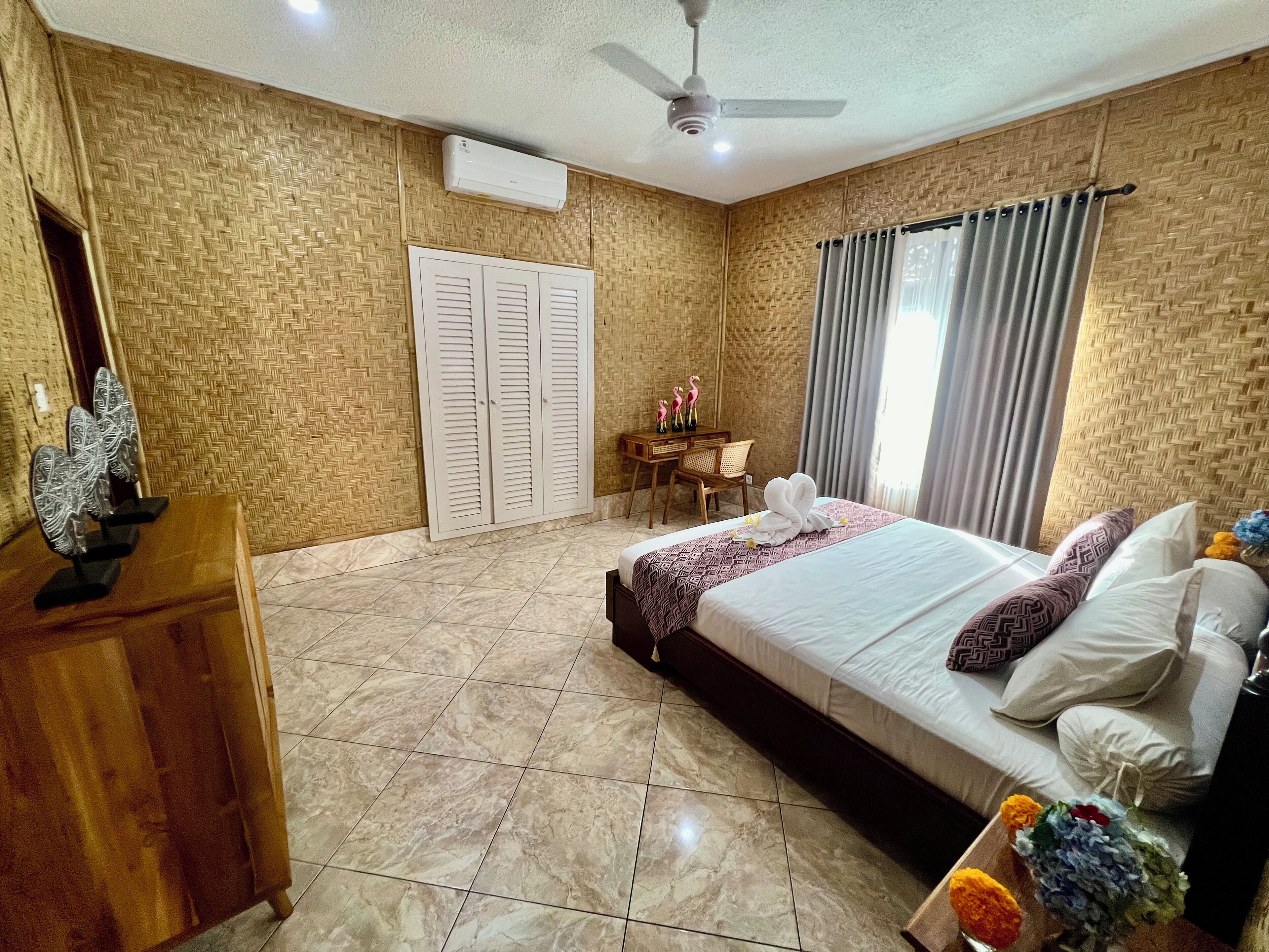 A hotel room with a bed, a desk, a chair, a wardrobe, and a ceiling fan.