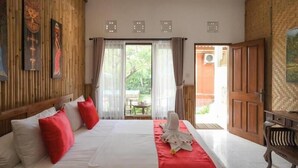 A hotel room with a bed, a wooden headboard, a red and white bedspread, and a view of the outside. - Villa Tiga Naga Sanur (Denpasar)