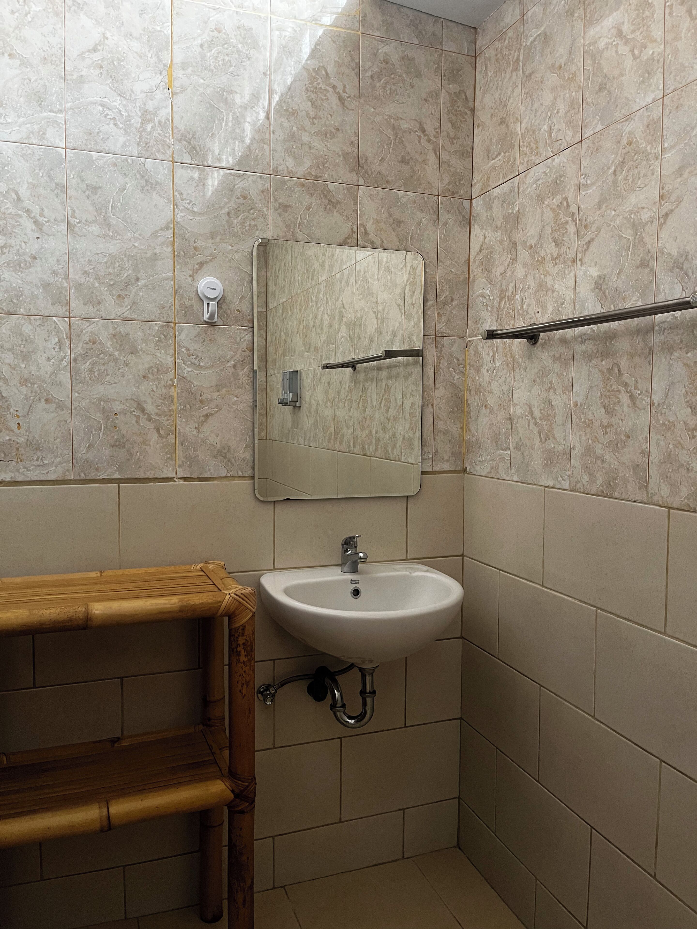 A bathroom with a marble-tiled wall, a white sink, a mirror, and a towel rack.