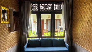 A room with a blue sofa, a glass-top table with a chessboard, and a view of a garden through a window with decorative lattice. - Villa Tiga Naga Sanur (Denpasar)