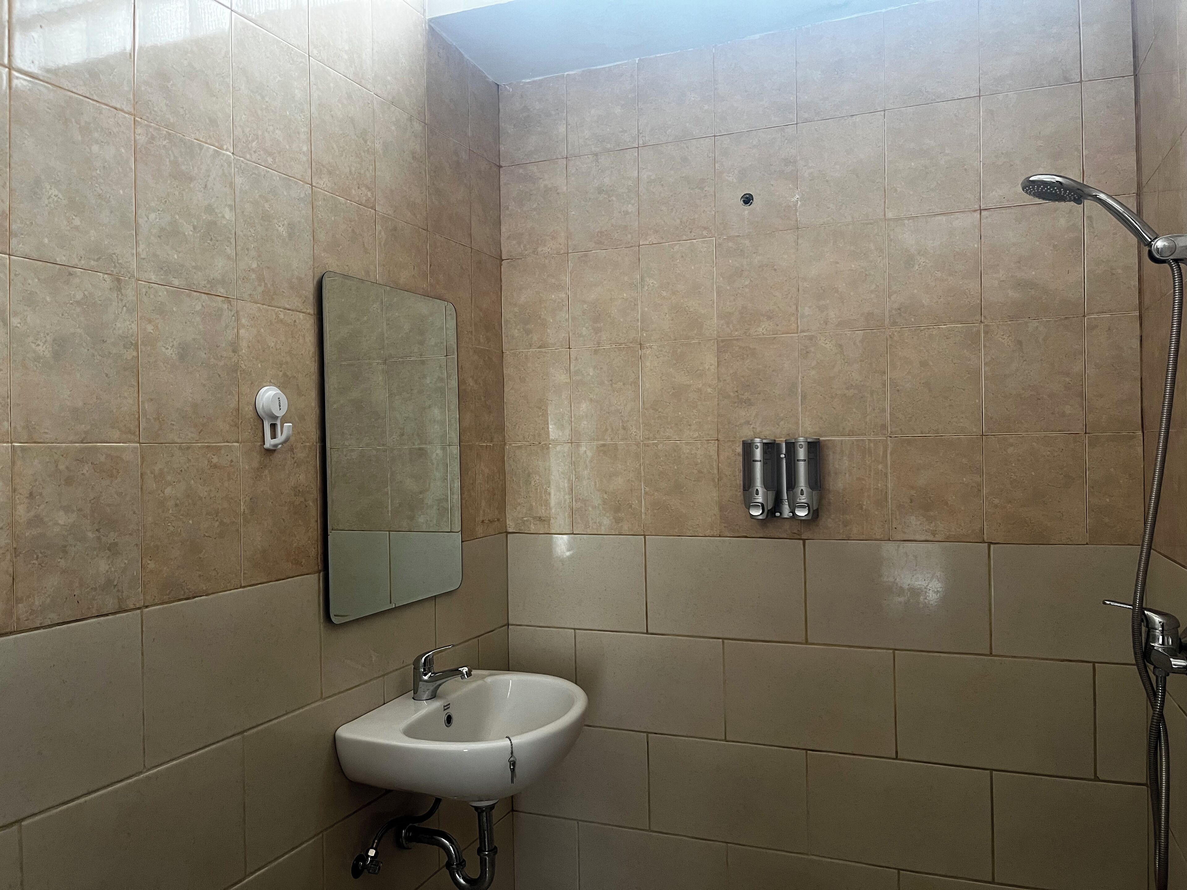 Ein Badezimmer mit beige farbenen Fliesen, einem weißen Waschbecken, einem Spiegel und einer Dusche.